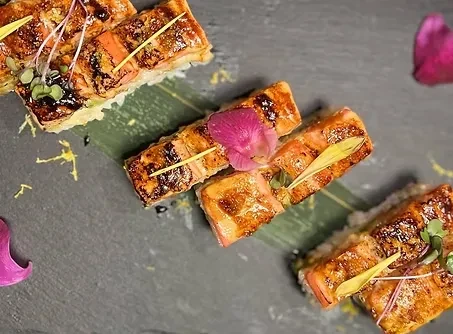 Seared sushi rolls on rice, garnished with microgreens and flowers.