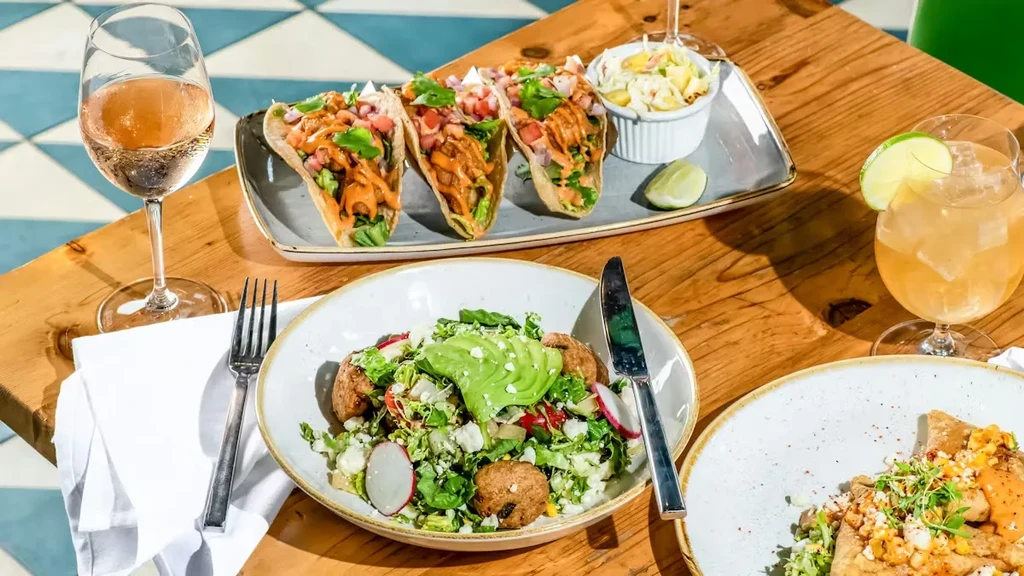 Table with tacos, salad, savory dish, wine, and a cocktail.