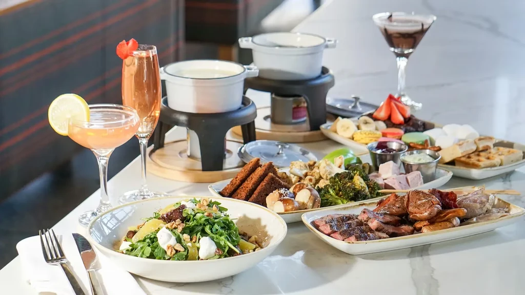 Fondue pots surrounded by various platters of food, salad, and cocktails.