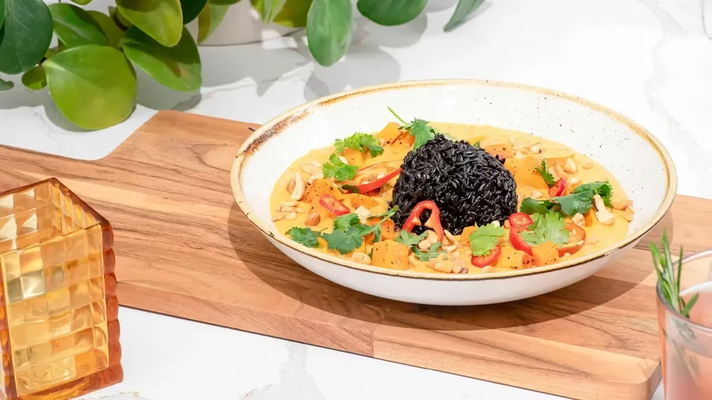 Plated curry with orange sauce, black rice, squash, and garnishes.