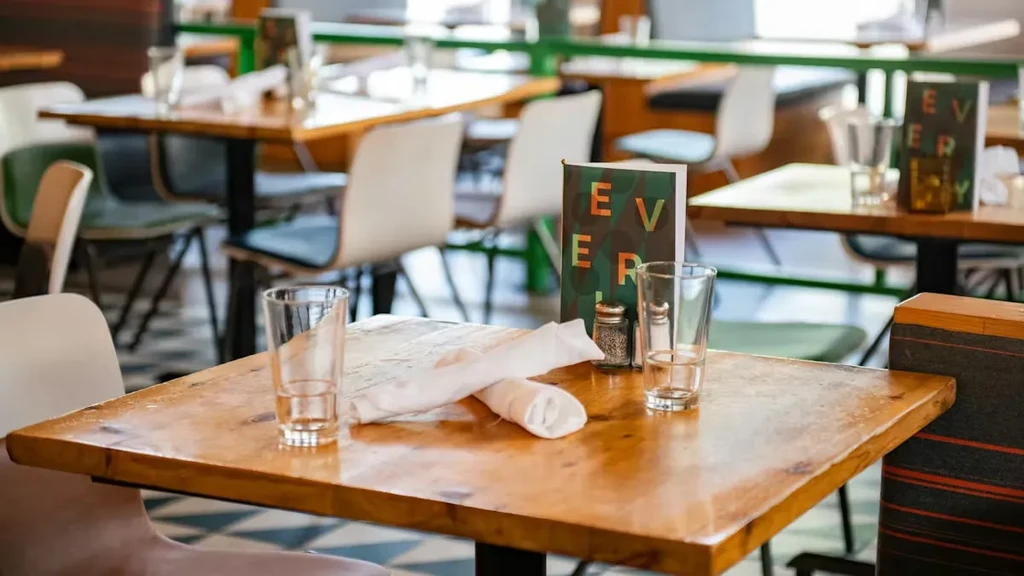 Bright restaurant interior, set table with glasses, menu, salt and pepper.