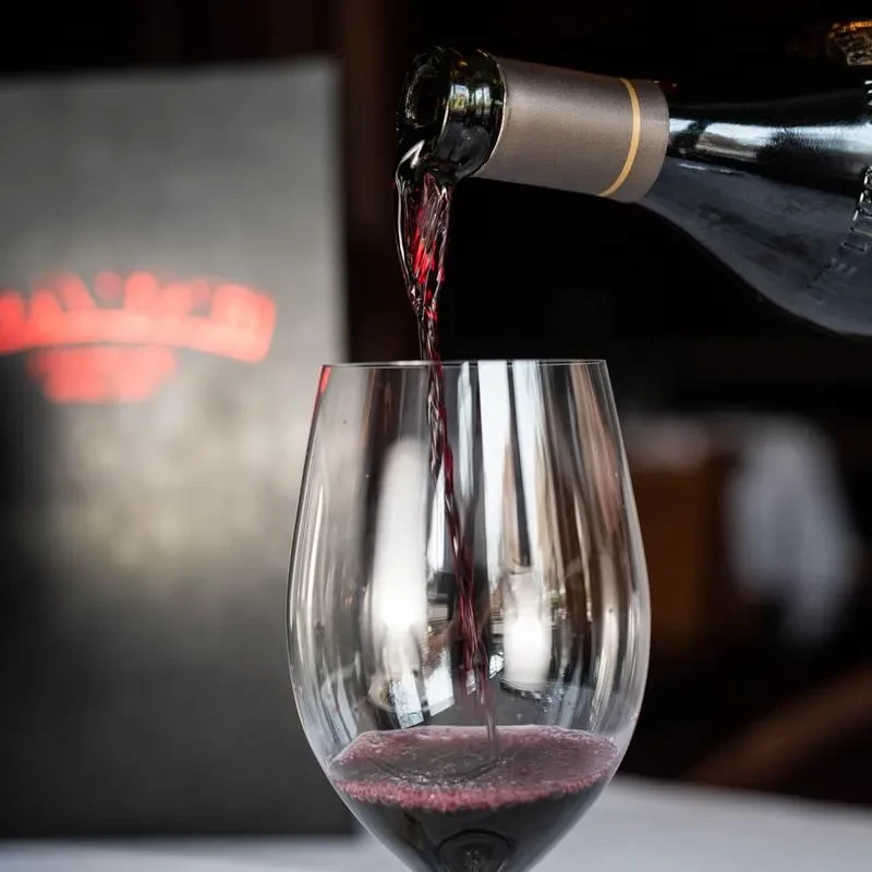 Dark red wine pours from bottle into glass, creating froth.