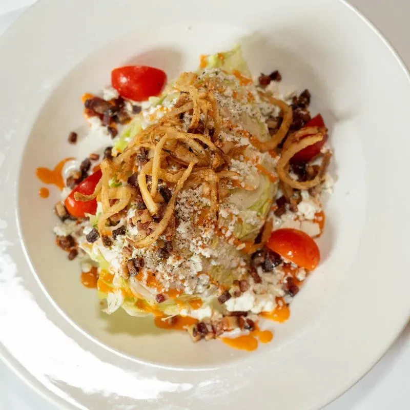 Close-up, top-down wedge salad with blue cheese, bacon, tomatoes, fried onions.