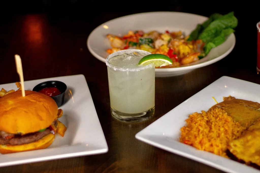 A restaurant spread of burger, margarita, rice, and stir-fry.