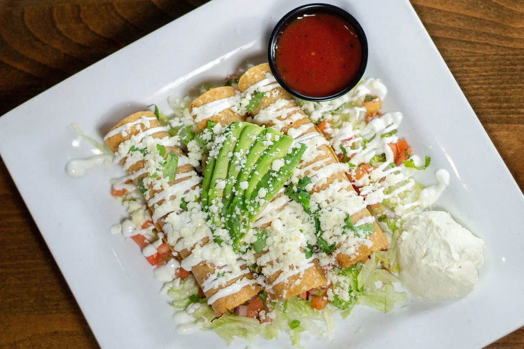 Top-down of Mexican flautas with avocado, cheese, crema, and salsa.