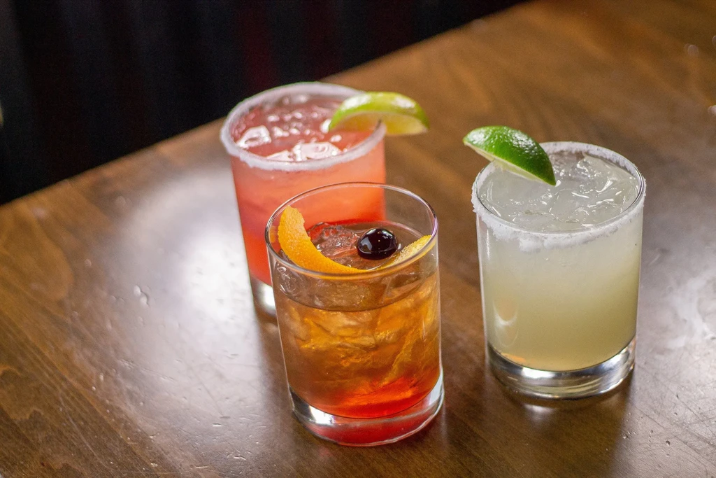 Pink, amber, and green cocktails on a rustic wooden surface.
