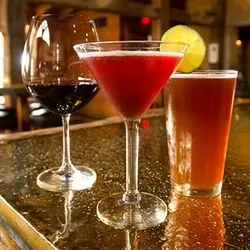 Red wine, a red cocktail, and beer on a bar top.