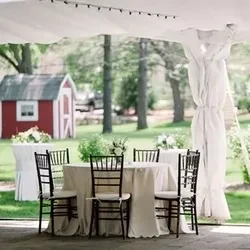Outdoor dining table and chairs under a white event tent.