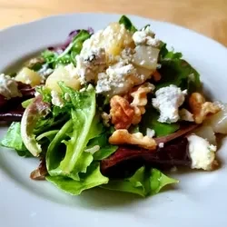 Green salad topped with blue cheese, pear pieces, and walnuts.