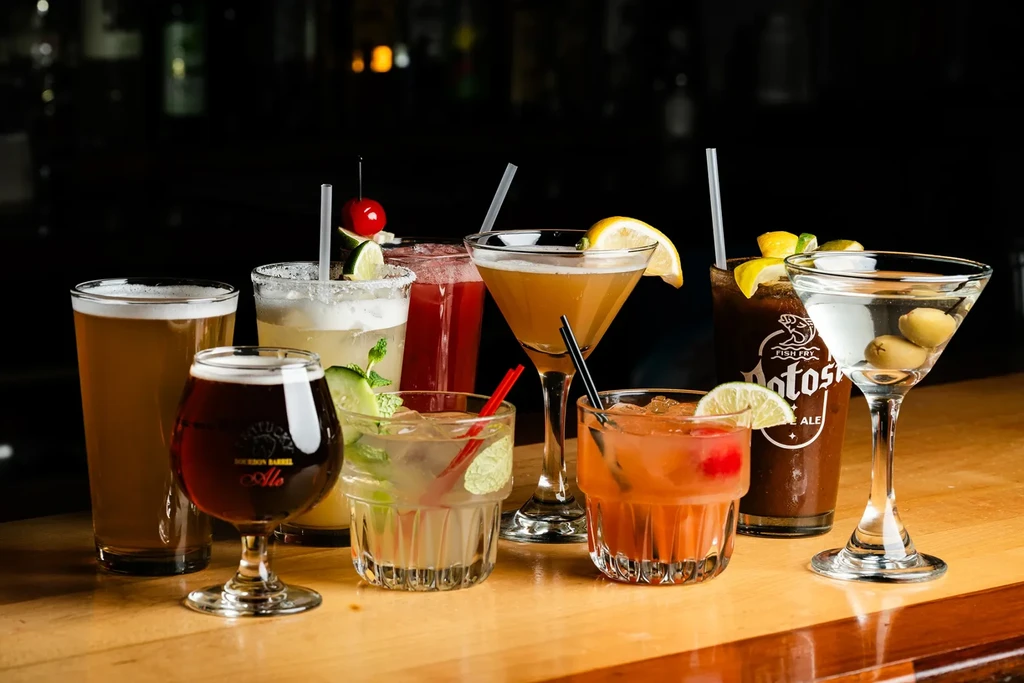 Eight distinct beers and cocktails on a polished wooden bar counter.