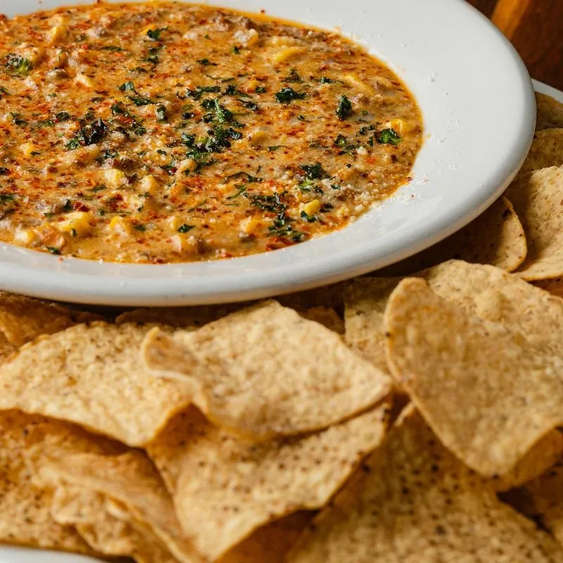 Cheesy dip with corn, herbs, and spices, with tortilla chips.