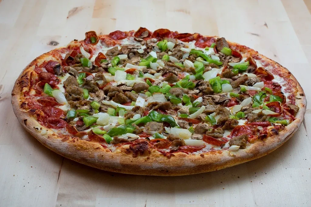 Pizza with pepperoni, sausage, peppers, onions, mushrooms on wood.