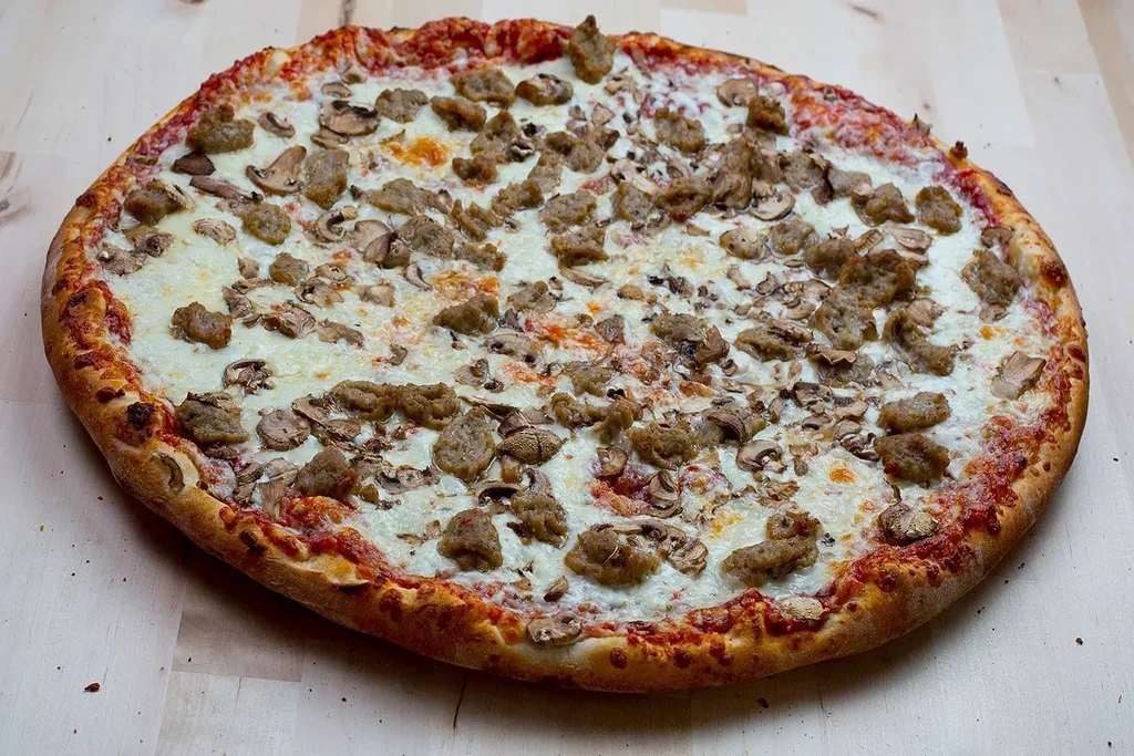 A whole round pizza with golden crust, sausage, mushrooms, and melted cheese.