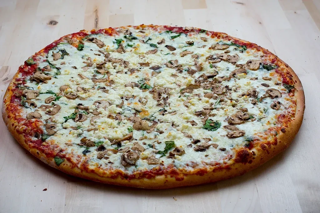 Round pizza heavily topped with cheese, mushrooms, and green leaves.