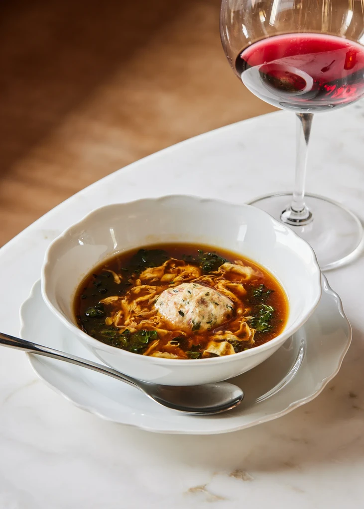 Bowl of amber soup with dumpling, herbs, and red wine.