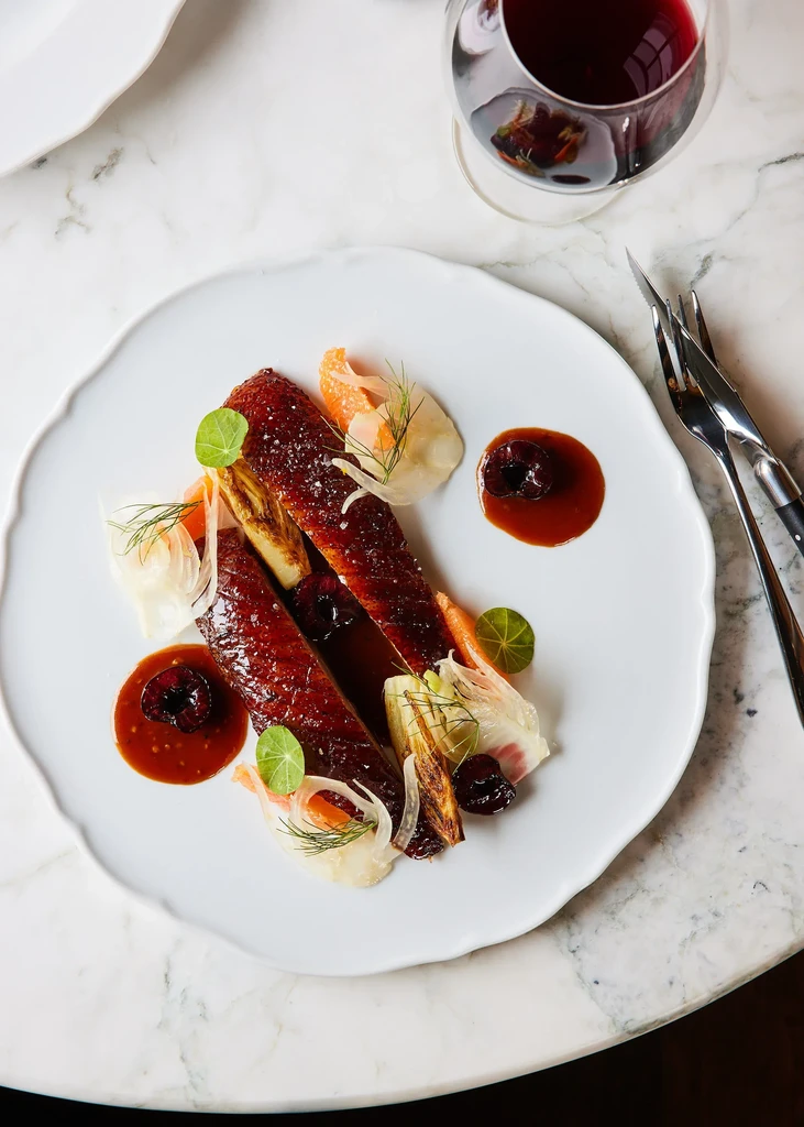 Slices of roasted poultry, colorful garnishes, dark sauce, and red wine.