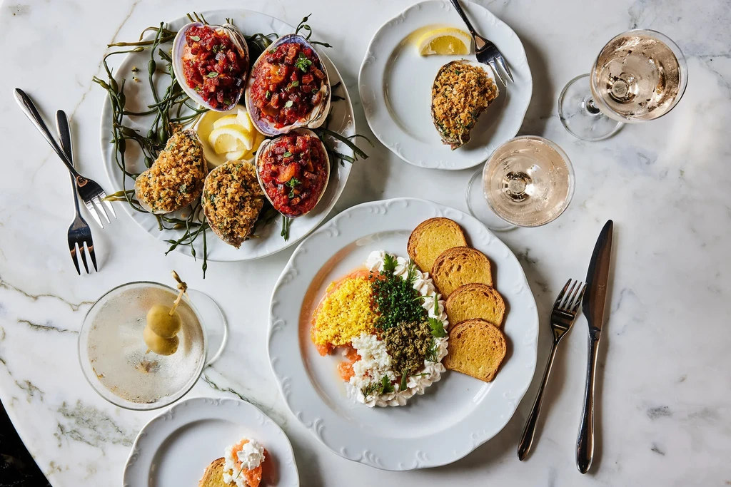 Overhead of appetizers, shellfish, and drinks on a white marble table.