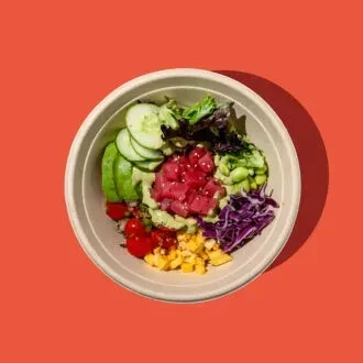 Colorful poke bowl with tuna, vegetables, and avocado on an orange background.
