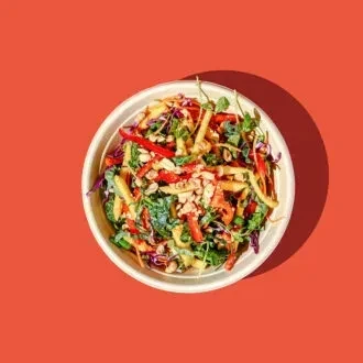 Colorful salad with greens, peppers, cabbage, nuts in bowl on red.