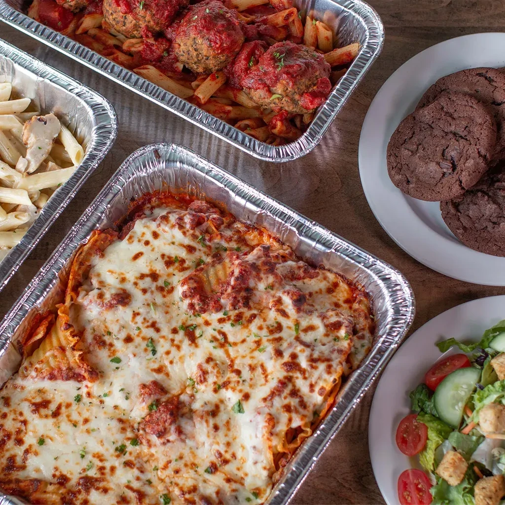 Catering spread of Italian pasta, meatballs, ziti, salad, and cookies.