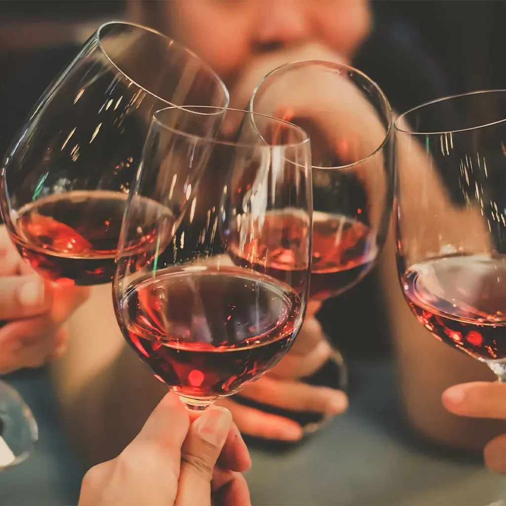 Four red wine glasses clinking in a toast, held by hands.