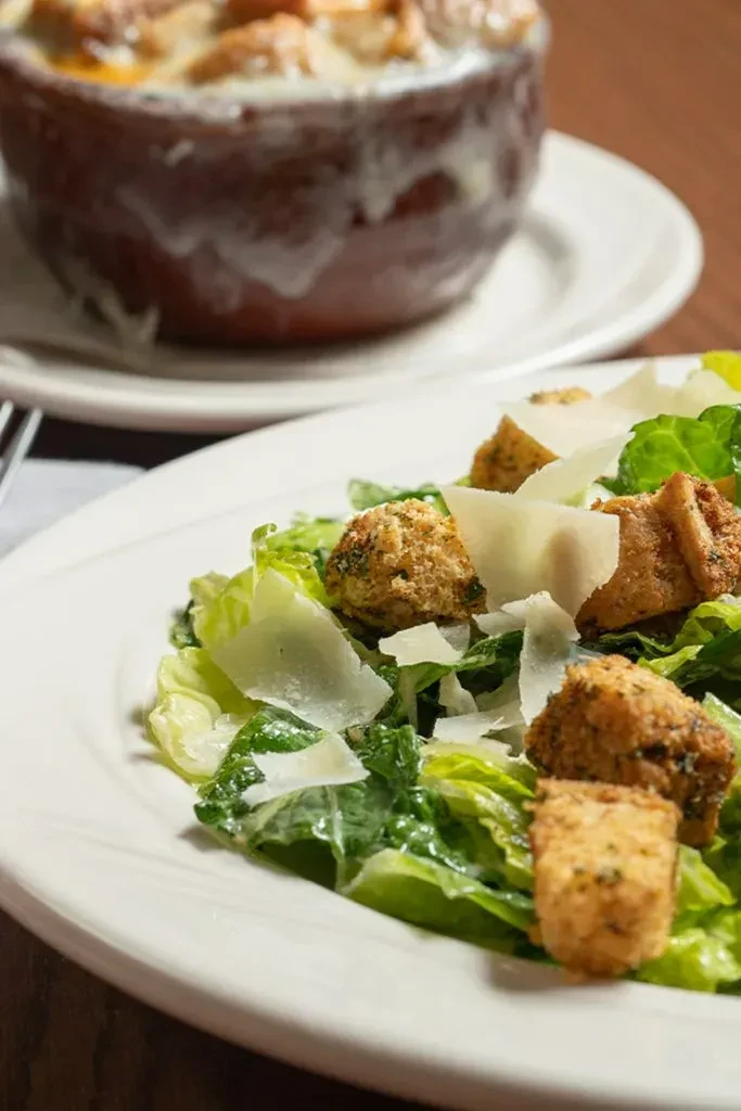 Crisp Caesar salad with a baked cheese dish on a dark table.