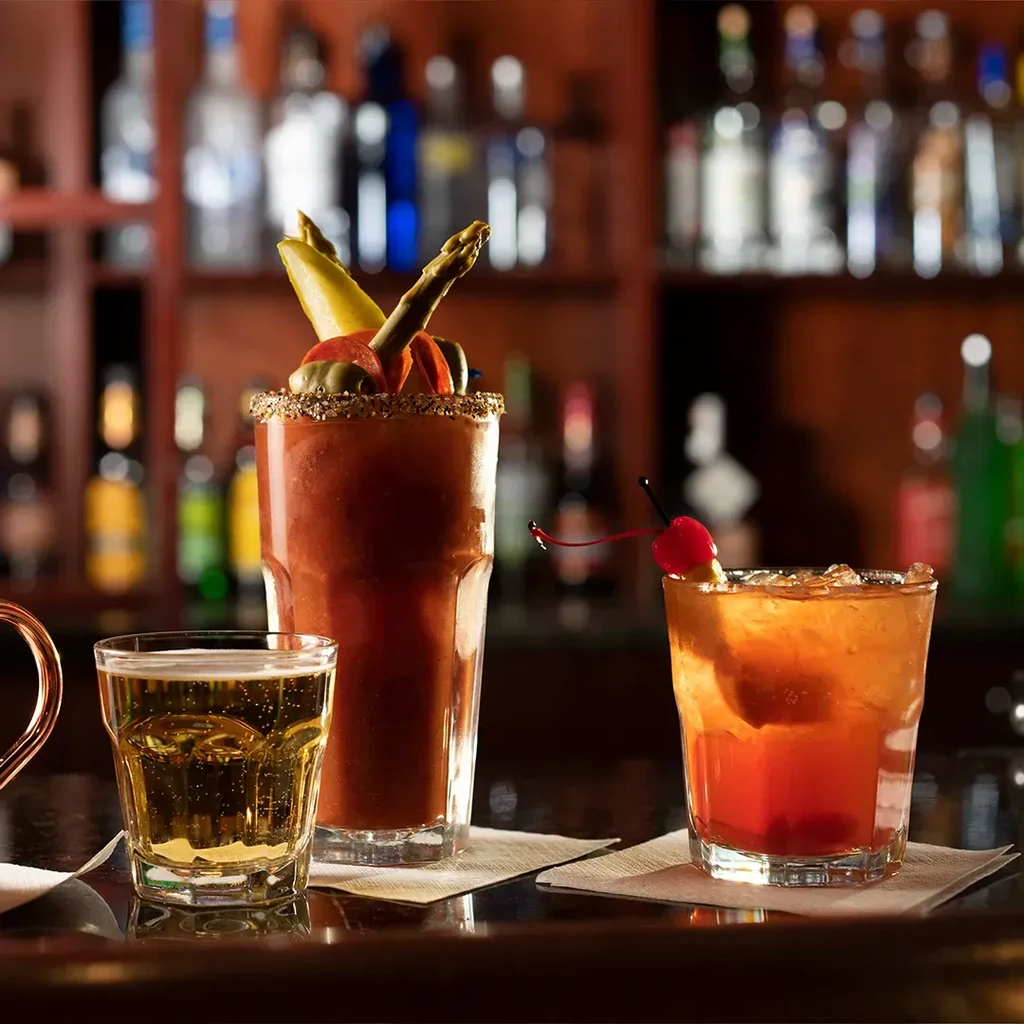 Three varied drinks, one elaborately garnished, on a bar with spirit bottles.