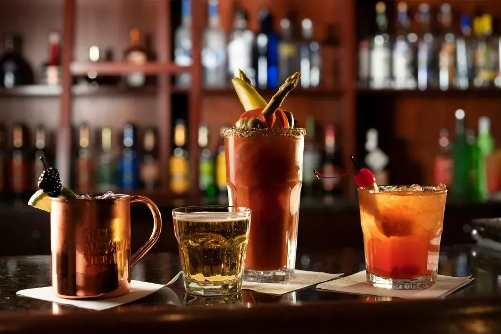 Four diverse, garnished cocktails on a dark bar counter.