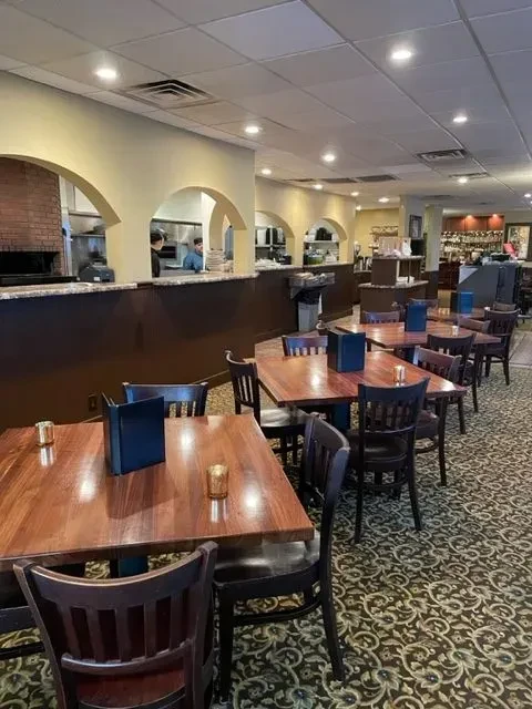 Restaurant dining room with wooden tables, a brick oven, and a bar.