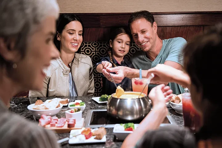 Family of four smiling, eating fondue at a restaurant table.