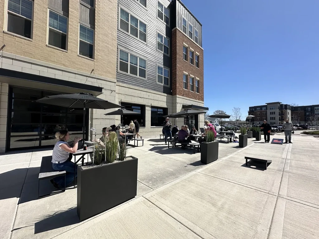 Restaurant patio with people dining and playing cornhole on a sunny day.