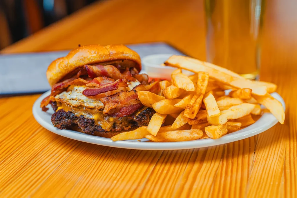 Burger with cheese, bacon, egg, and fries on a wooden table.
