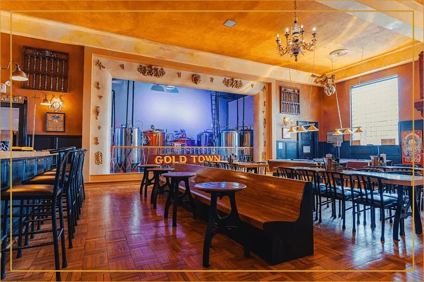 Industrial-chic brewery restaurant interior with bar, seating, and illuminated brewing vats.