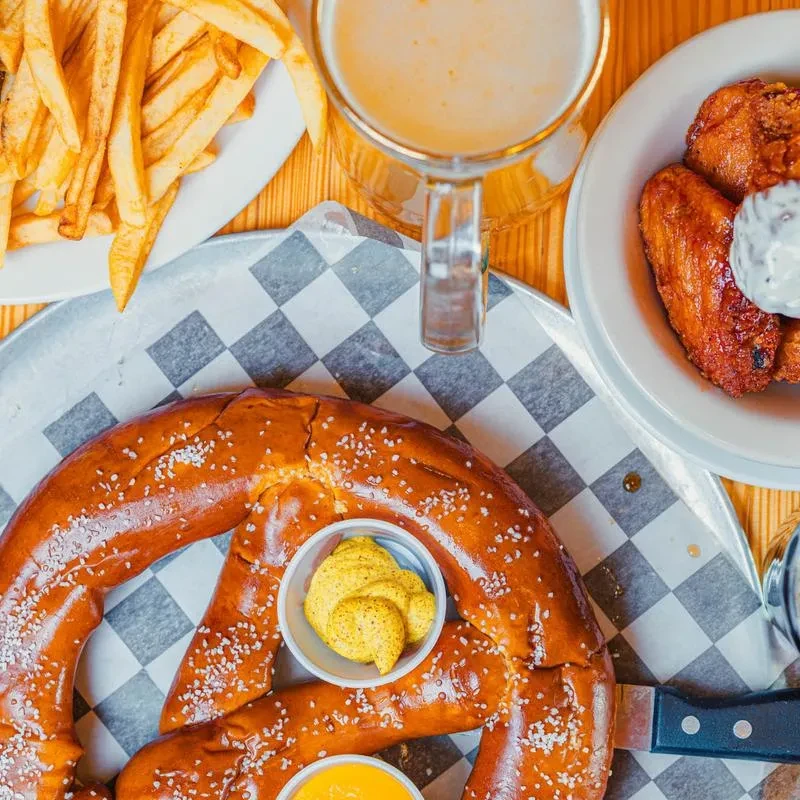 Overhead view of large pretzel with dips, fries, beer, and wings.