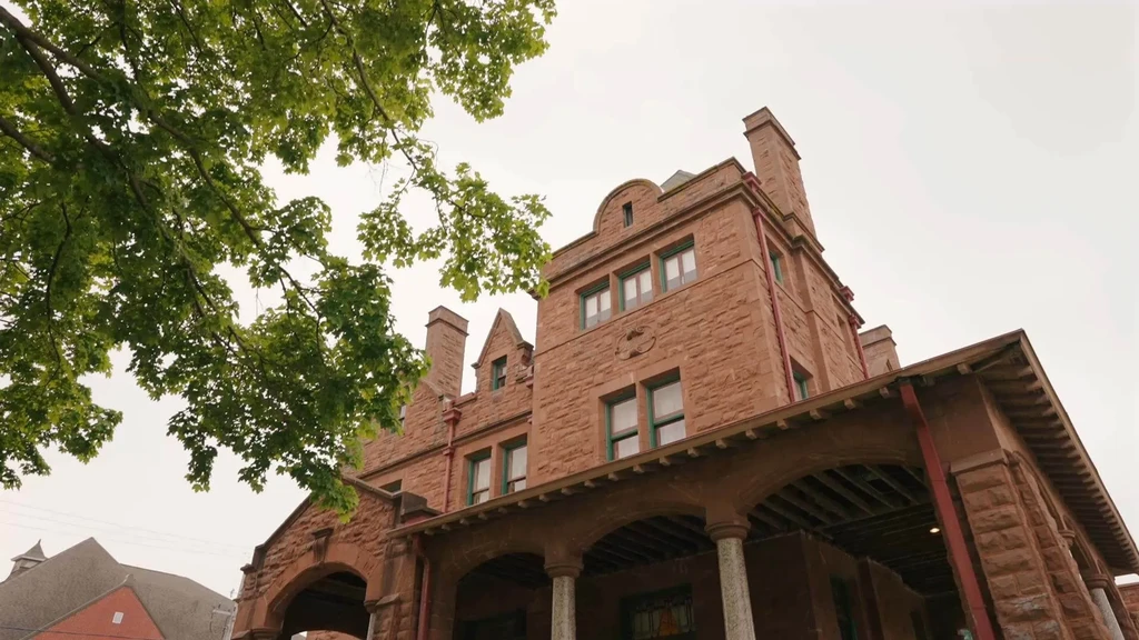 Historic reddish-brown stone building with large covered porch, chimneys, arched windows.