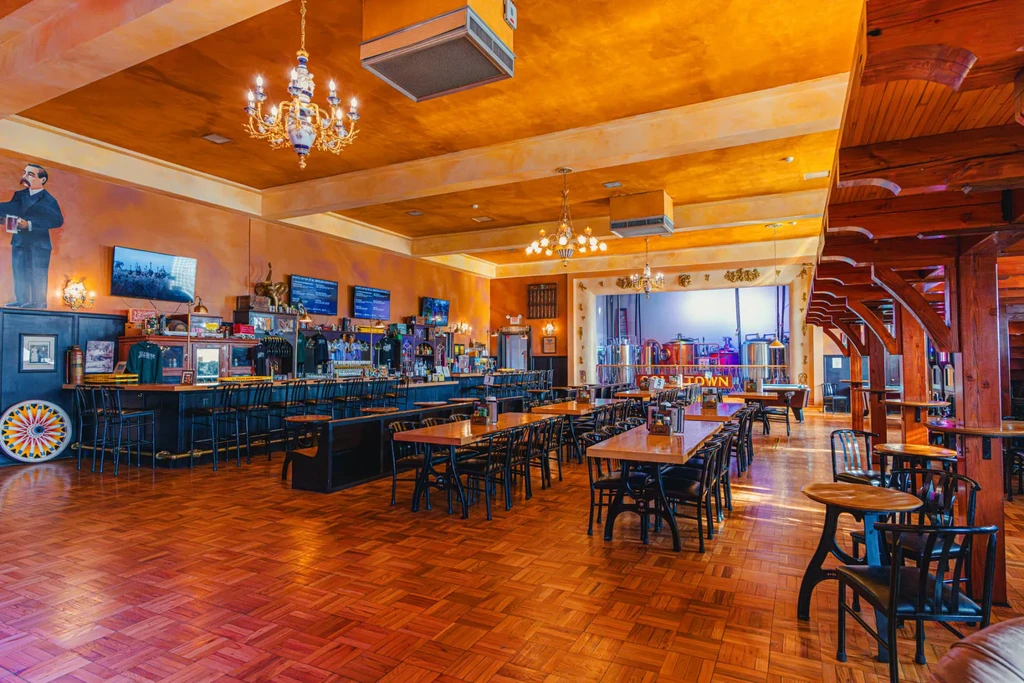Empty, warmly lit brewery interior with bar, tables, and stainless tanks.