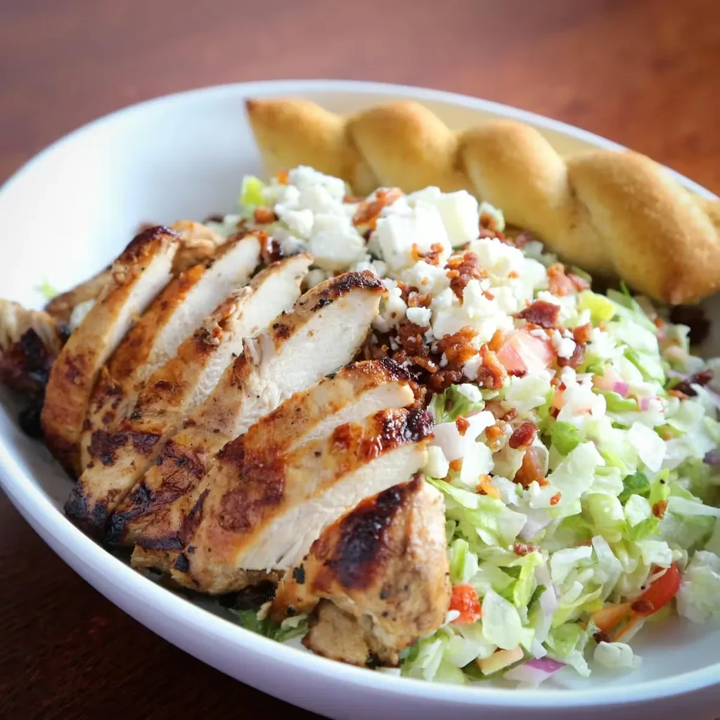 Grilled chicken salad with crumbled cheese, bacon, and breadstick.