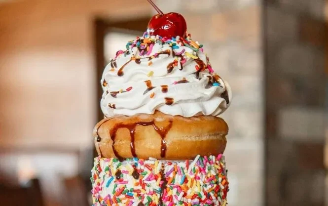 Extreme milkshake dessert with donut, whipped cream, sprinkles, and cherry.