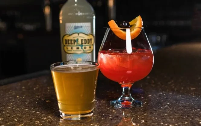 Amber drink, Deep Eddy Lemon bottle, and red cocktail on bar.