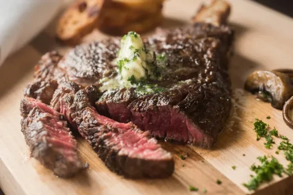 Sliced medium-rare steak with melting herb butter on a wooden board.