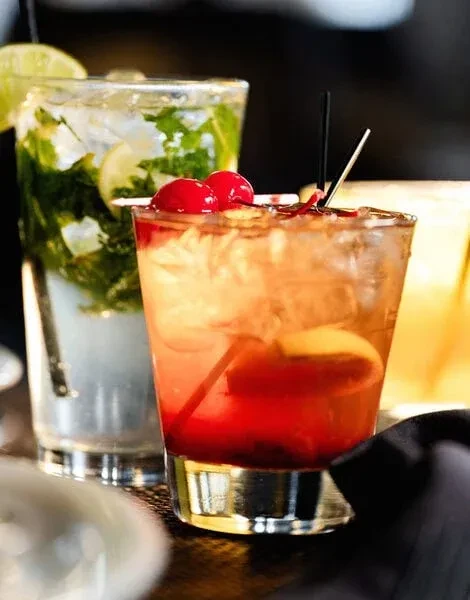 Two cocktails: red-orange with cherries, green mojito with mint and lime.