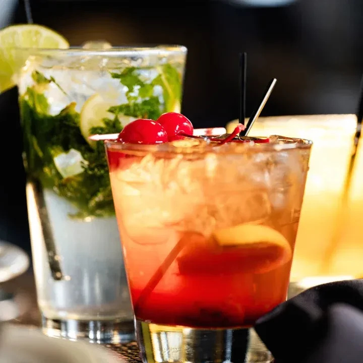 Two cocktails: a reddish-orange drink with cherries and a green mojito.