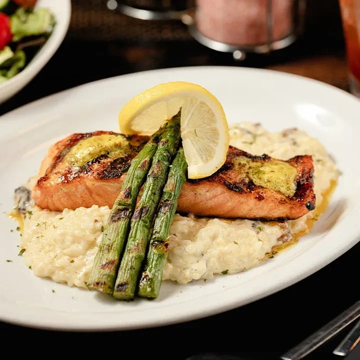 Grilled salmon fillets, risotto, asparagus, and lemon on a white plate.