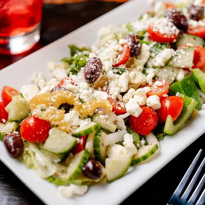 Fresh salad with cucumber, tomatoes, olives, and feta on a white plate.