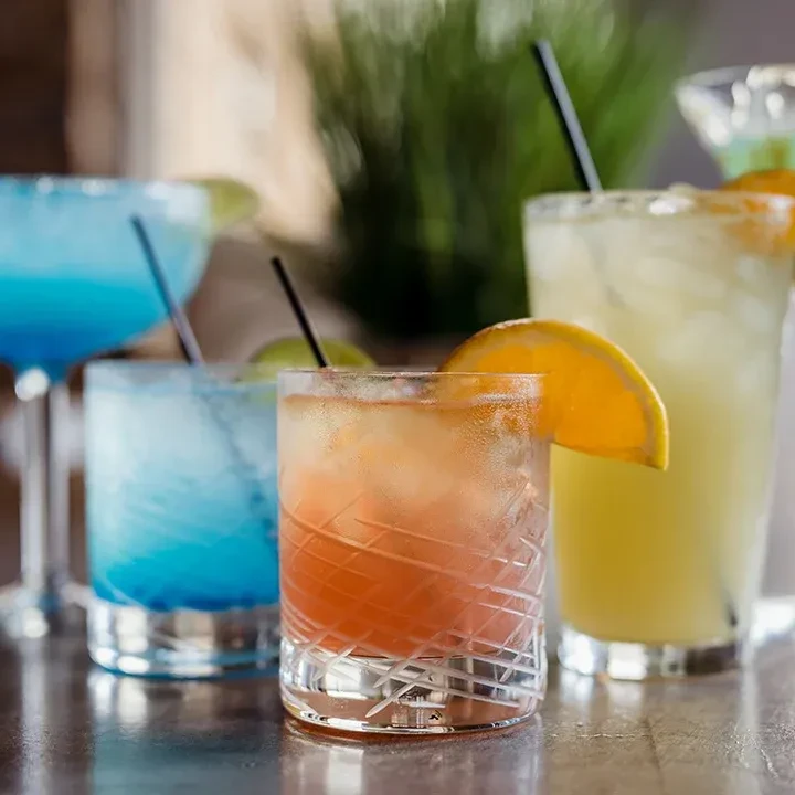 Colorful iced cocktails with fruit on a bar, green foliage background.