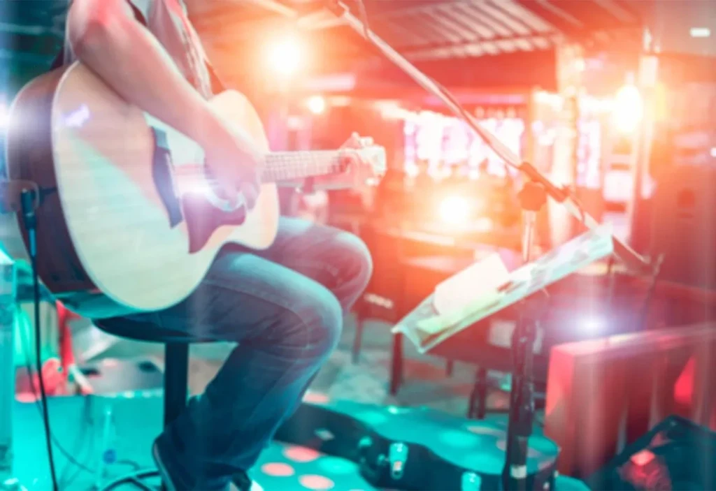 Blurred musician plays acoustic guitar with colorful lights and flares.
