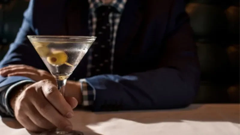 Person in suit holds frosted martini with green olive.