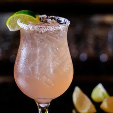 Peachy-pink cocktail with ice, a textured rim, and a lime wedge.