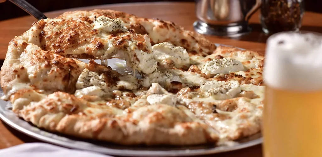 Round white pizza with stretching cheese, ricotta, and herbs.