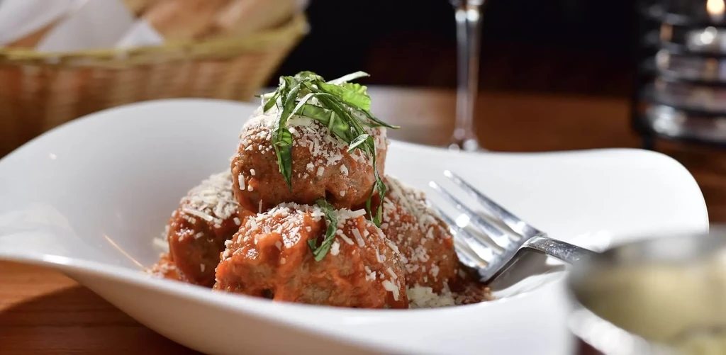 Close-up dish of meatballs with red sauce, cheese, and herbs.